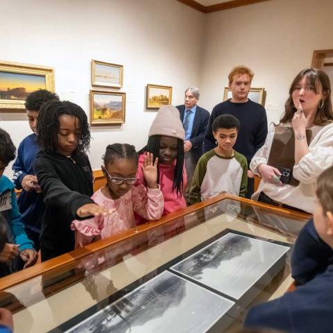 Students gathered around a glass case in a museum looking in.