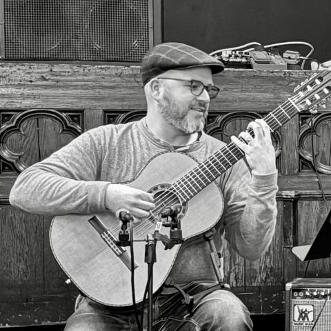 Trevor Babb plays classical guitar in a black-and-white photograph.