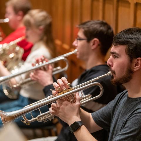 Student musicians play trumpet and other brass instruments during an orchestra performance.
