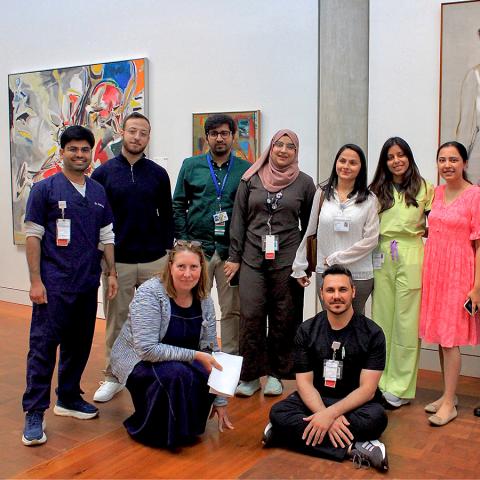 A group of nine people standing or sitting in an art museum with paintings on the walls.