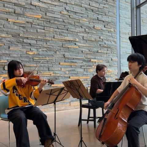 Three student musicians perform on violin, cello, and piano in the Bridge for Laboratory Sciences.