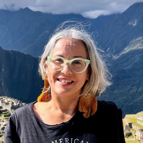 Catherine Ramírez smiling outdoors with mountains and ancient stone ruins behind her.