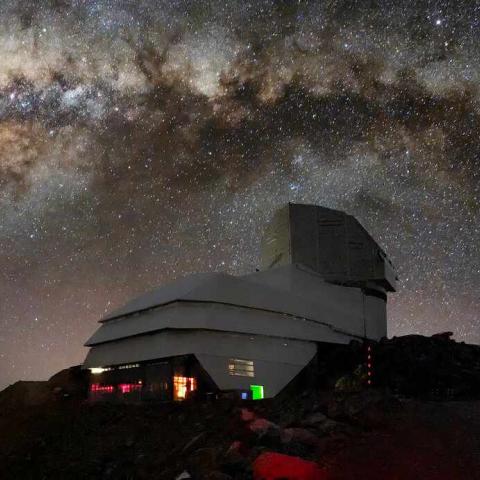 An observatory sits against a starry night sky, a galaxy visible in the background.