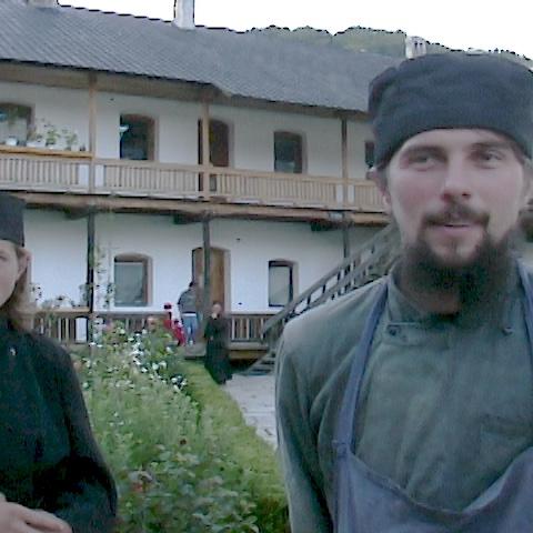 Two monks outside a building talking to a camera.