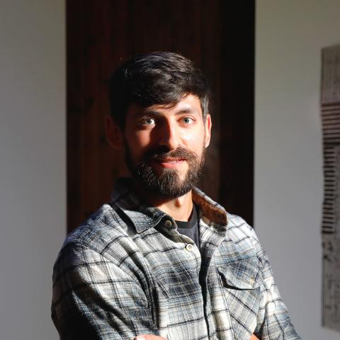 Person in a plaid shirt standing with arms crossed between two geometric artworks.