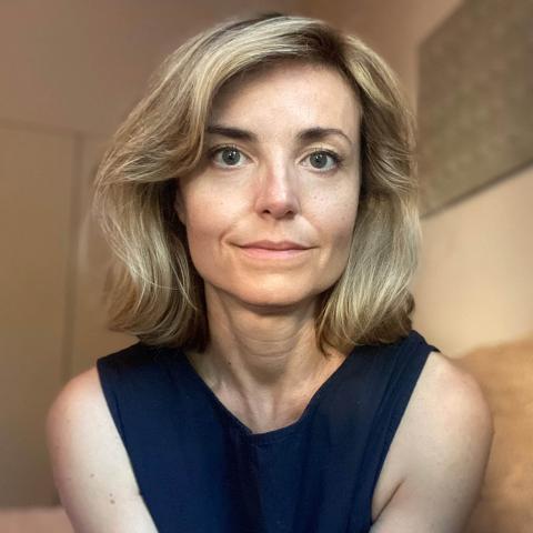 Portrait of a person with shoulder-length hair wearing a navy sleeveless top and looking at the camera.