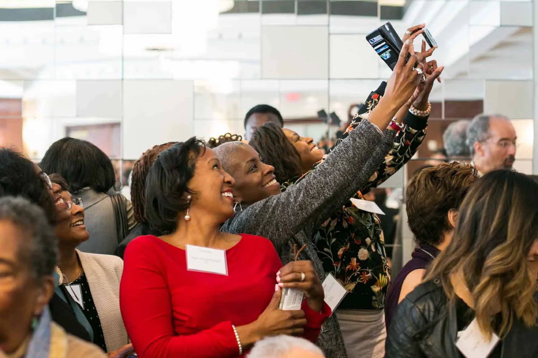 Several people take selfies at a crowded event.