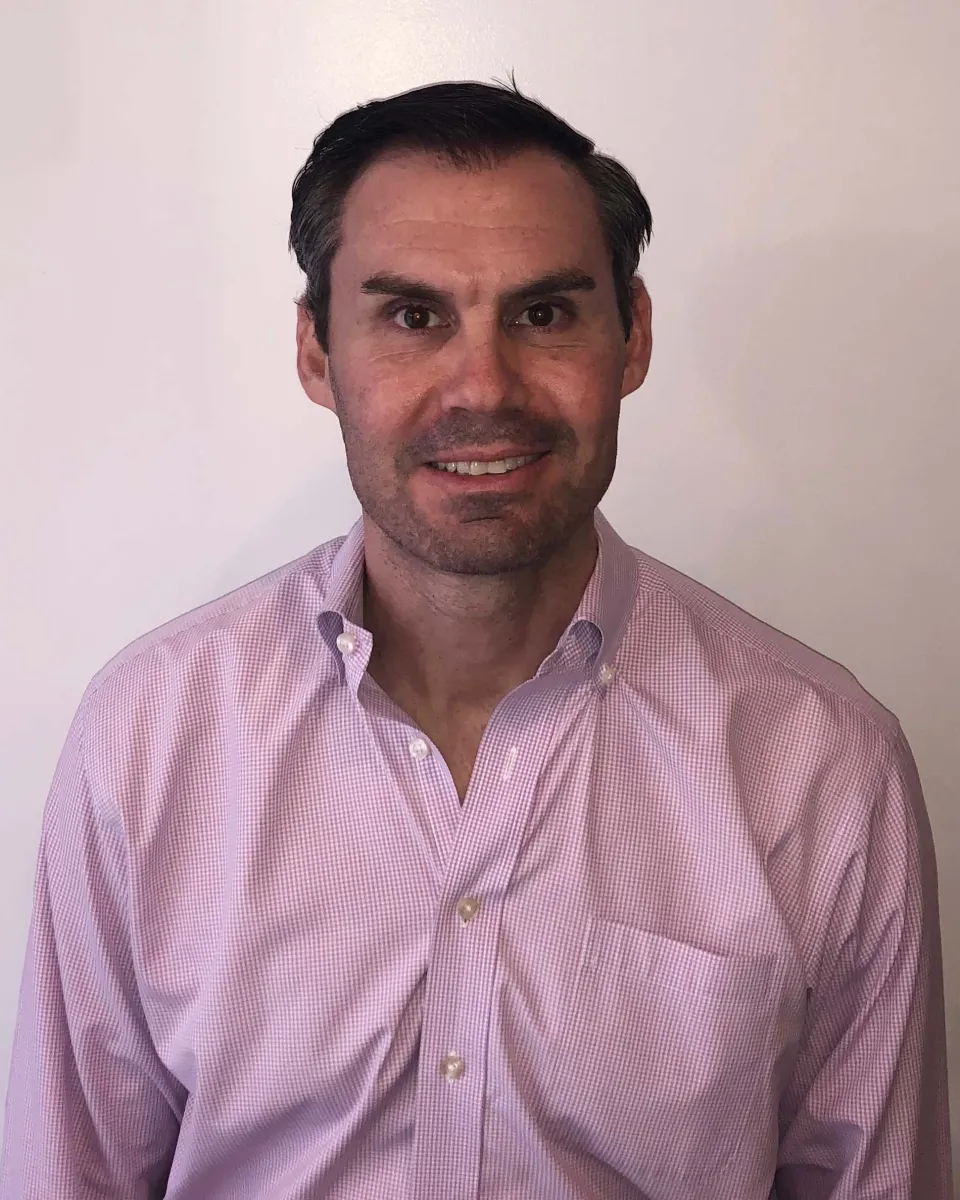 Person in a pink button-down shirt smiling against a plain background.
